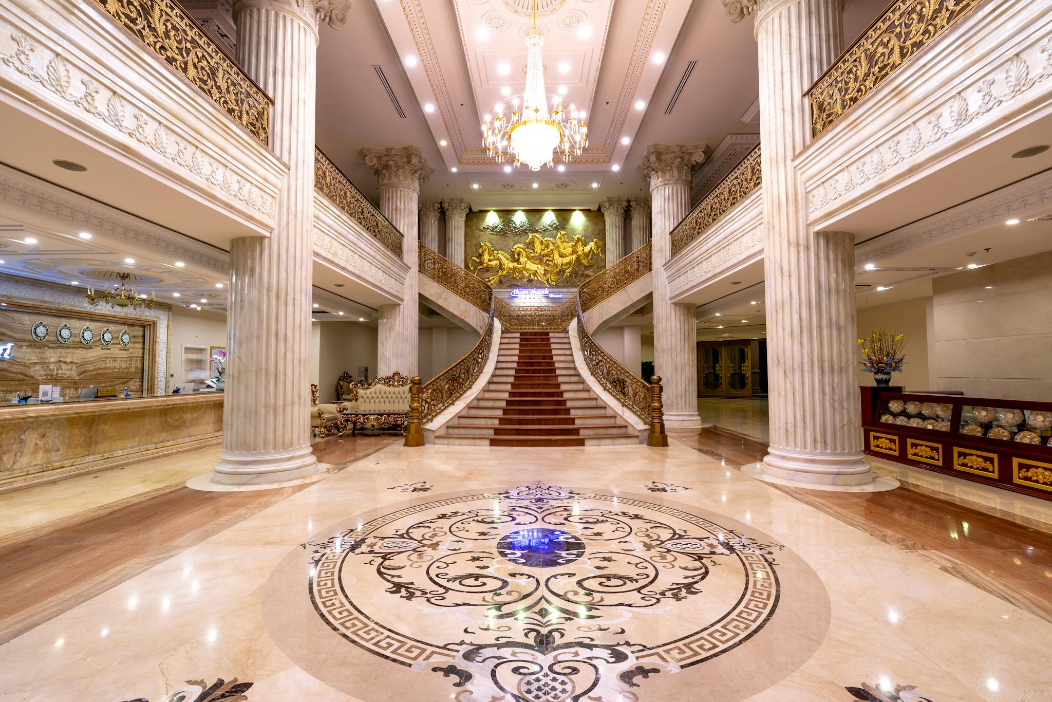 Elegant hotel foyer featuring a grand staircase, marble floors, and a dazzling chandelier.